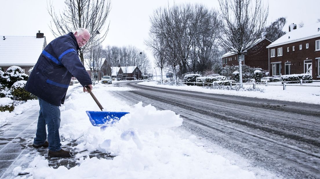 Een man schept de sneeuw van de stoep voor zijn huis in Alteveer