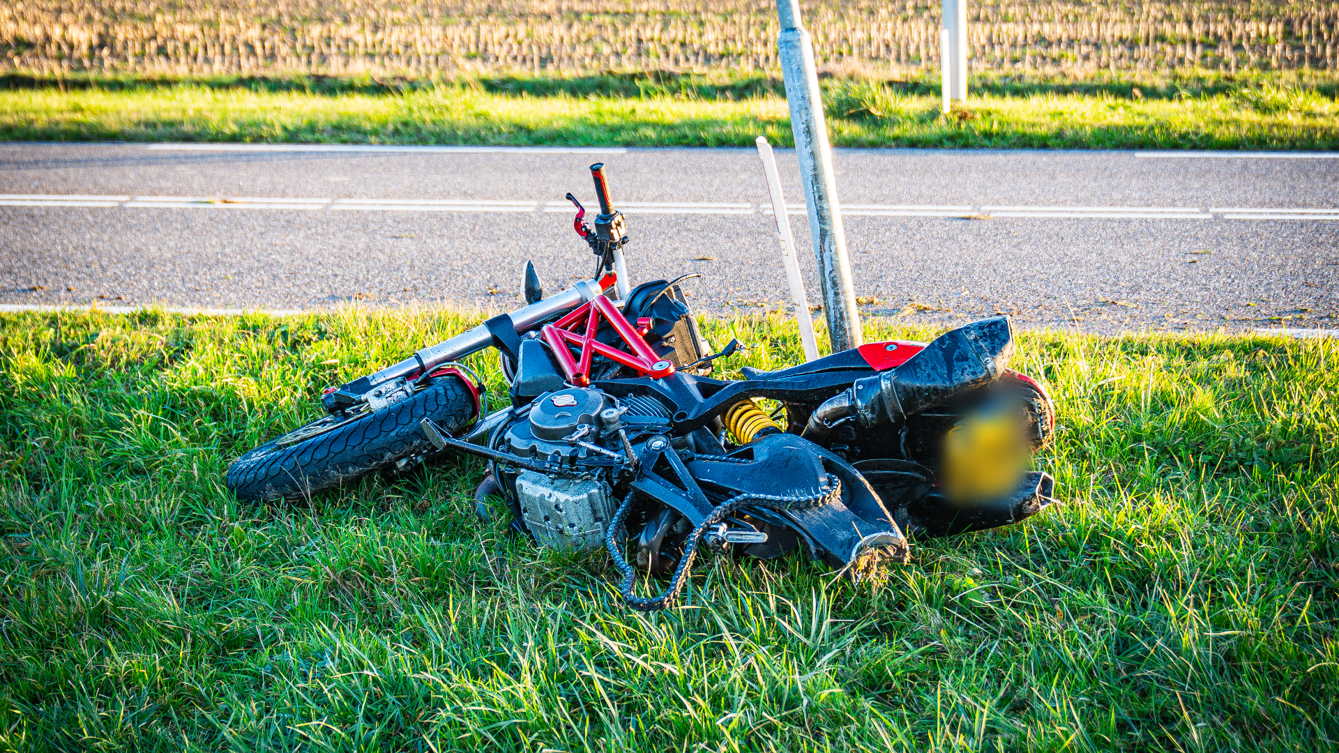 De motor is behoorlijk beschadigd in het gras terechtgekomen en mist een achterwiel dat verderop ligt.