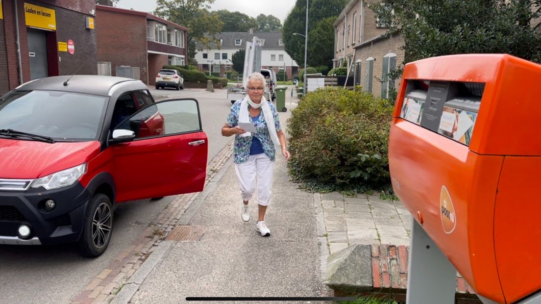 Een vrouw in een brommobiel heeft iets voor de brievenbus in Haren