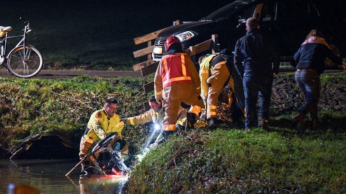 Nadat het slachtoffer op het droge is geholpen, halen hulpdiensten de fiets van de man uit de sloot.