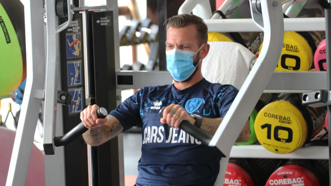 John Goossens met een mondkapje op een fitnessapparaat