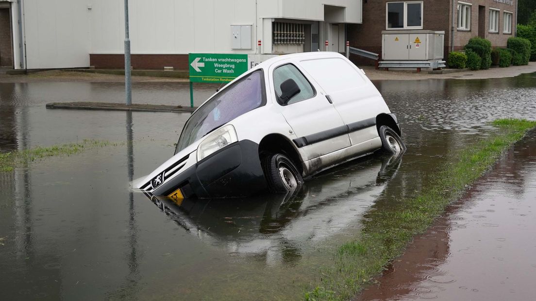Een auto in Dalfsen is deels onder water verdwenen na flinke regenval, vanmiddag.