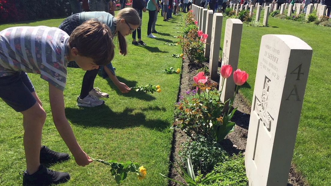 Kinderen leggen bloemen bij de Canadese begraafplaats