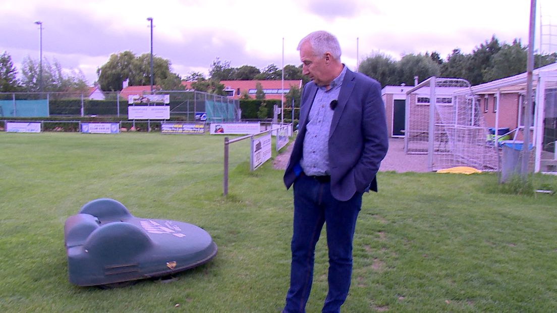 Wethouder Arno Witkam bekijkt de robotmaaier op het voetbalveld van Hoedekenskerke die op stroom rijdt, opgewerkt door zonnepanelen.