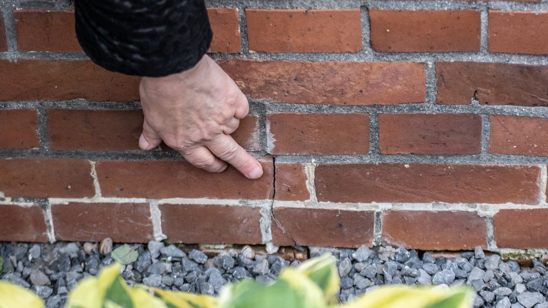 Een bewoner wijst een scheur in zijn muur aan