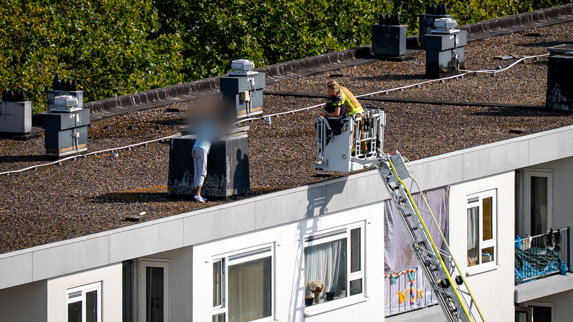 Een agent en brandweerman proberen de man naar beneden te krijgen.