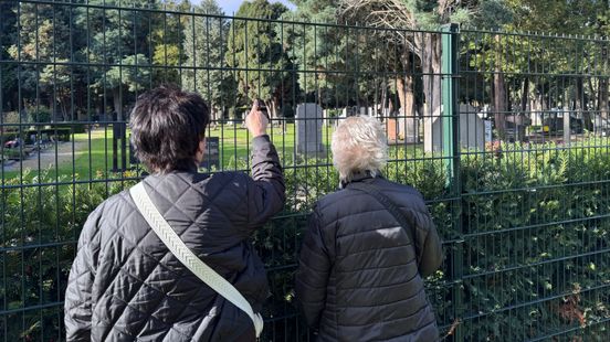 Begraafplaats dicht vanwege storm: bezoekers met bloemen staan voor een gesloten poort Home