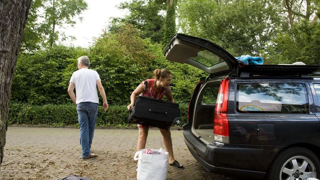 Een gezin laadt de auto vol voor vertrek naar vakantie.