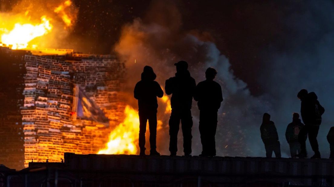 Bouwers kijken toe hoe de stapel in vlammen opgaat