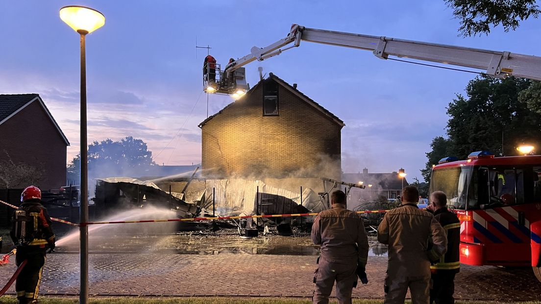 De brandweer blust met een hoogwerker het vuur dat is overgeslagen op de woning