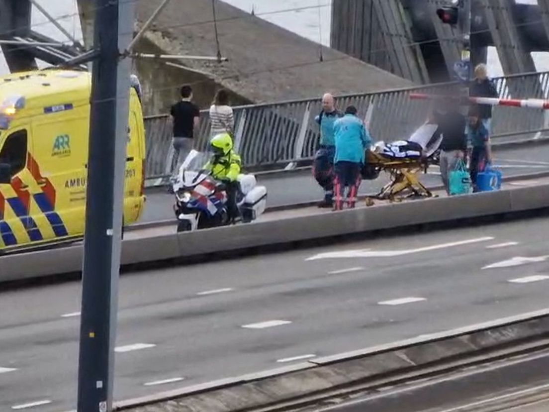 Bevallende vrouw op brancard onder slagbomen Erasmusbrug van ene naar andere ambulance