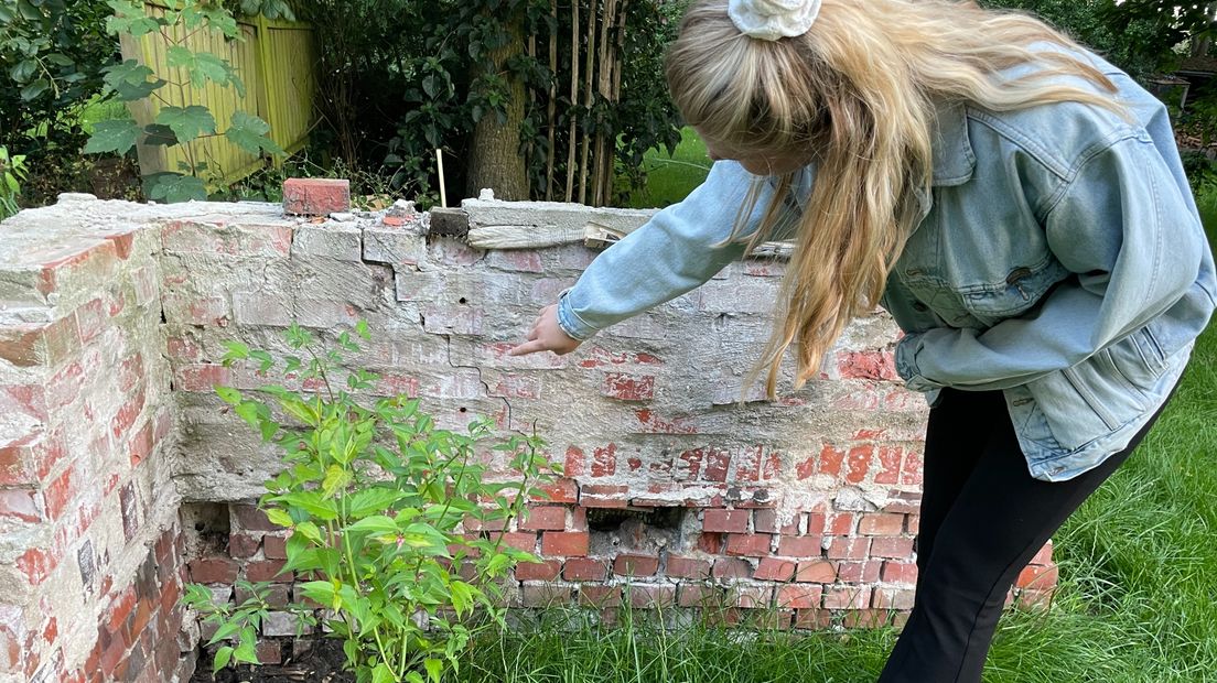 Een jonge Groningse wijst naar een scheur in de ruïne van haar oude huis