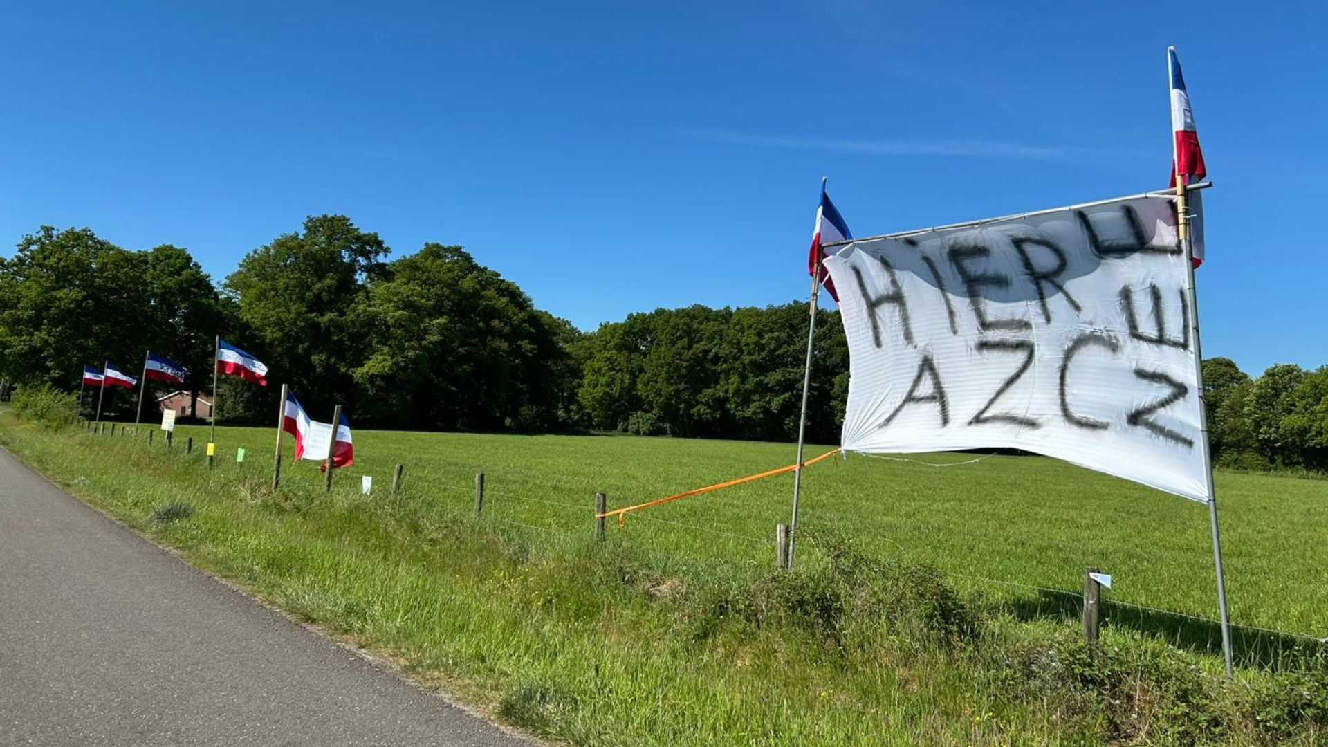 Een spandoek en protestvlaggen op de plek waar het AZC moet komen