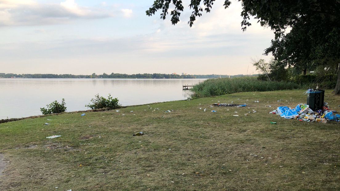 Tientallen flessen, blikjes en ander afval liggen verspreid rond het meer