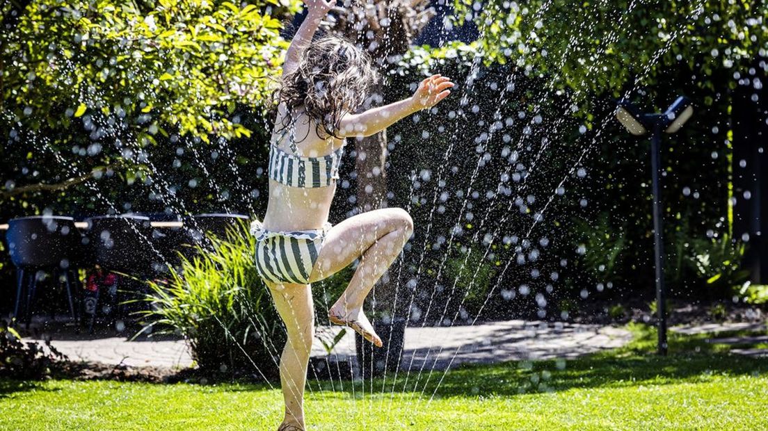 Een meisje speelt met water in een tuin.