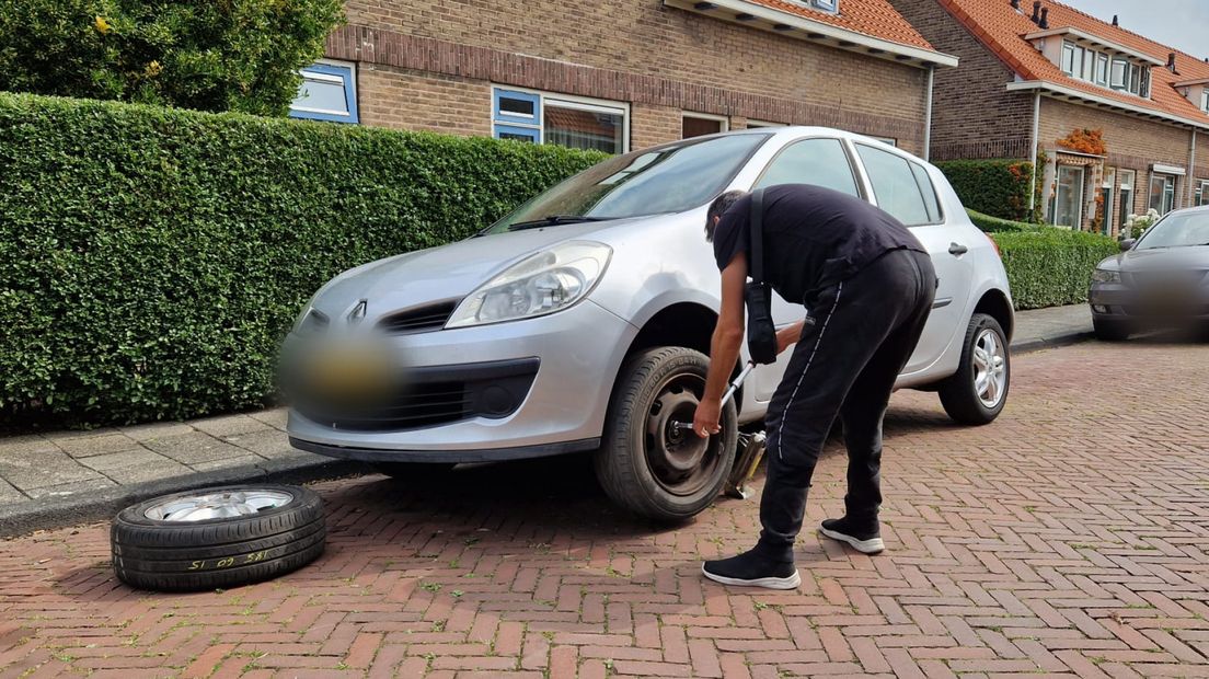 Een buurtbewoner is zijn lekgestoken band aan het vervangen