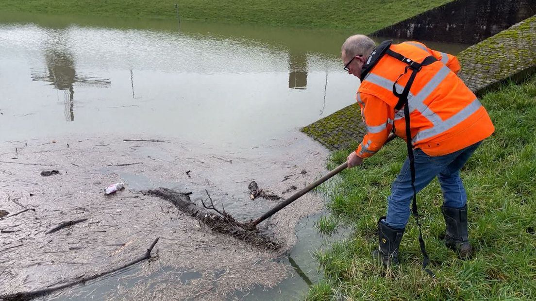 Dijkinspecteur ruimt rommel op in water bij dijk.