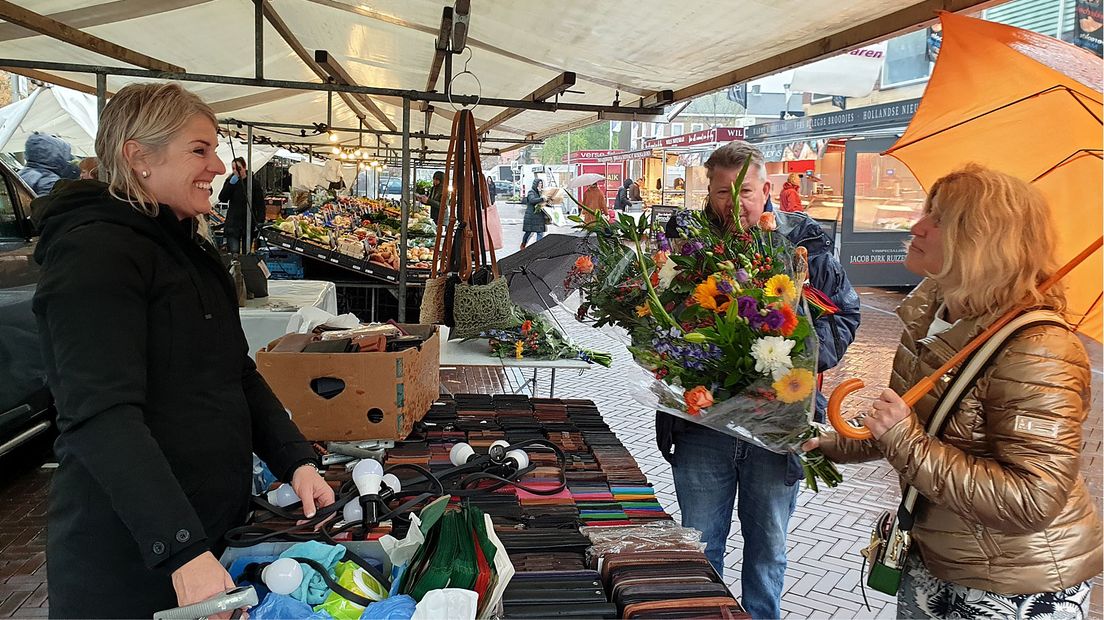 Wethouder en marktmeester delen bloemen uit op de markt.