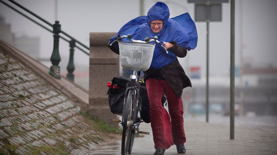 Een vrouw duwt op Scheveningen haar fiets tegen de wind en regen in