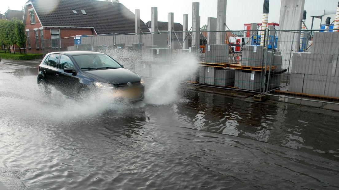 Een auto rijdt door het water na een enorme hoosbui