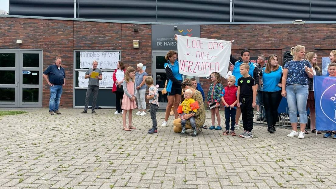 Zwembadpersoneel en kinderen met een spandoek met de tekst 'Laat ons niet verzuipen'