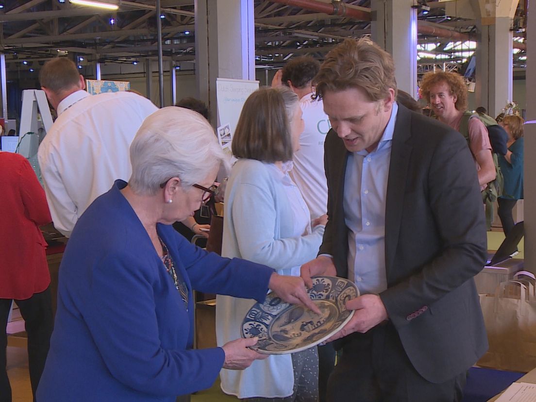 Een mevrouw komt met een Delfts blauw bord langs