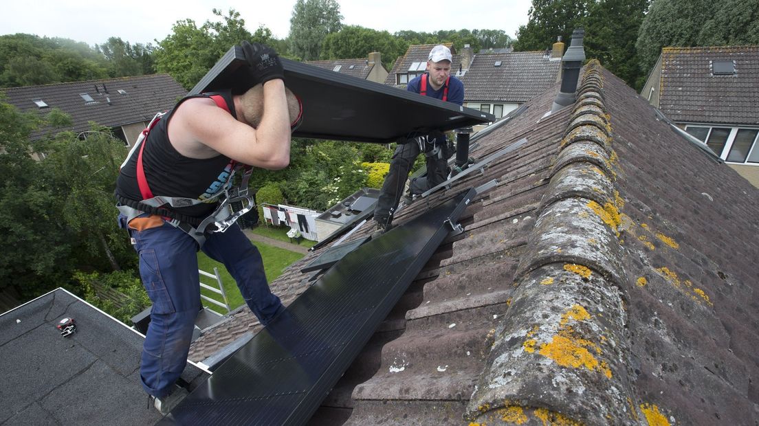 Twee mannen plaatsen zonnepanelen op een dak.