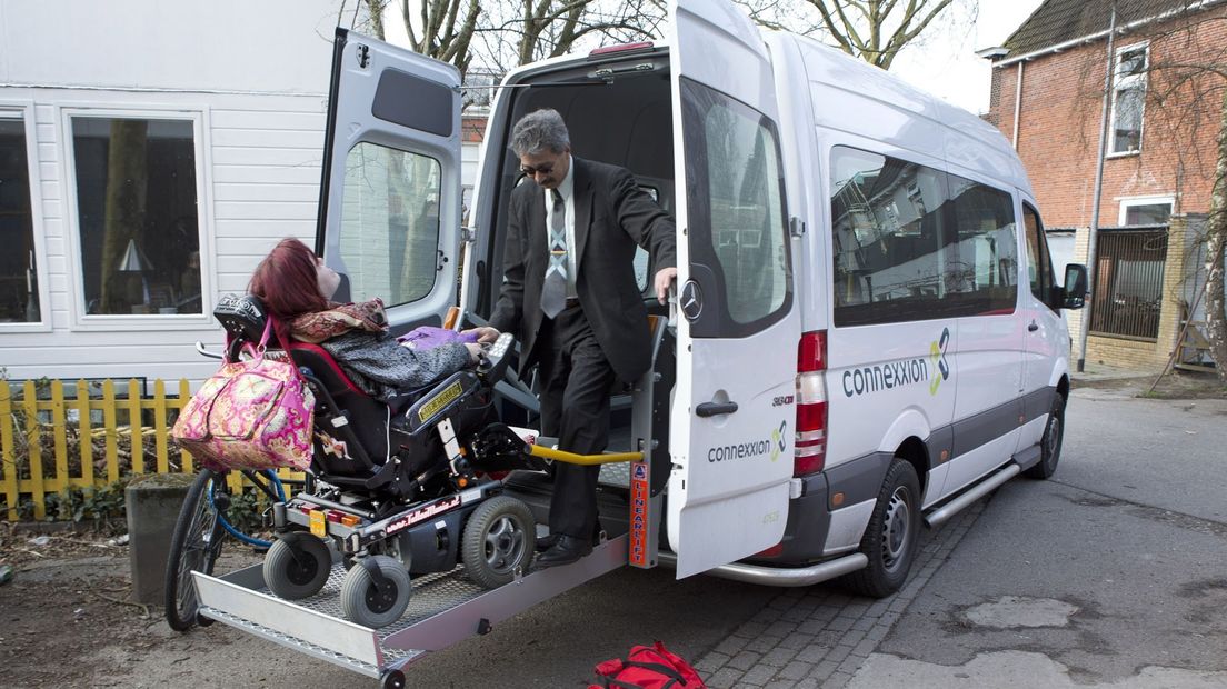Een chauffeur helpt een vrouw in een rolstoelbus (archief)