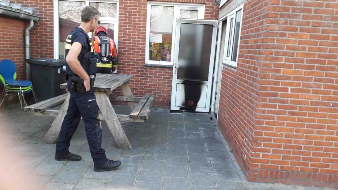 Een brandweerman inspecteert de zwartgeblakerde deur met het kattenluikje