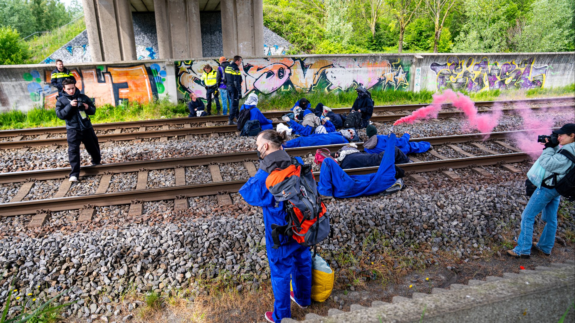 Demonstranten liggen op een stuk spoor dat onder een snelweg loopt