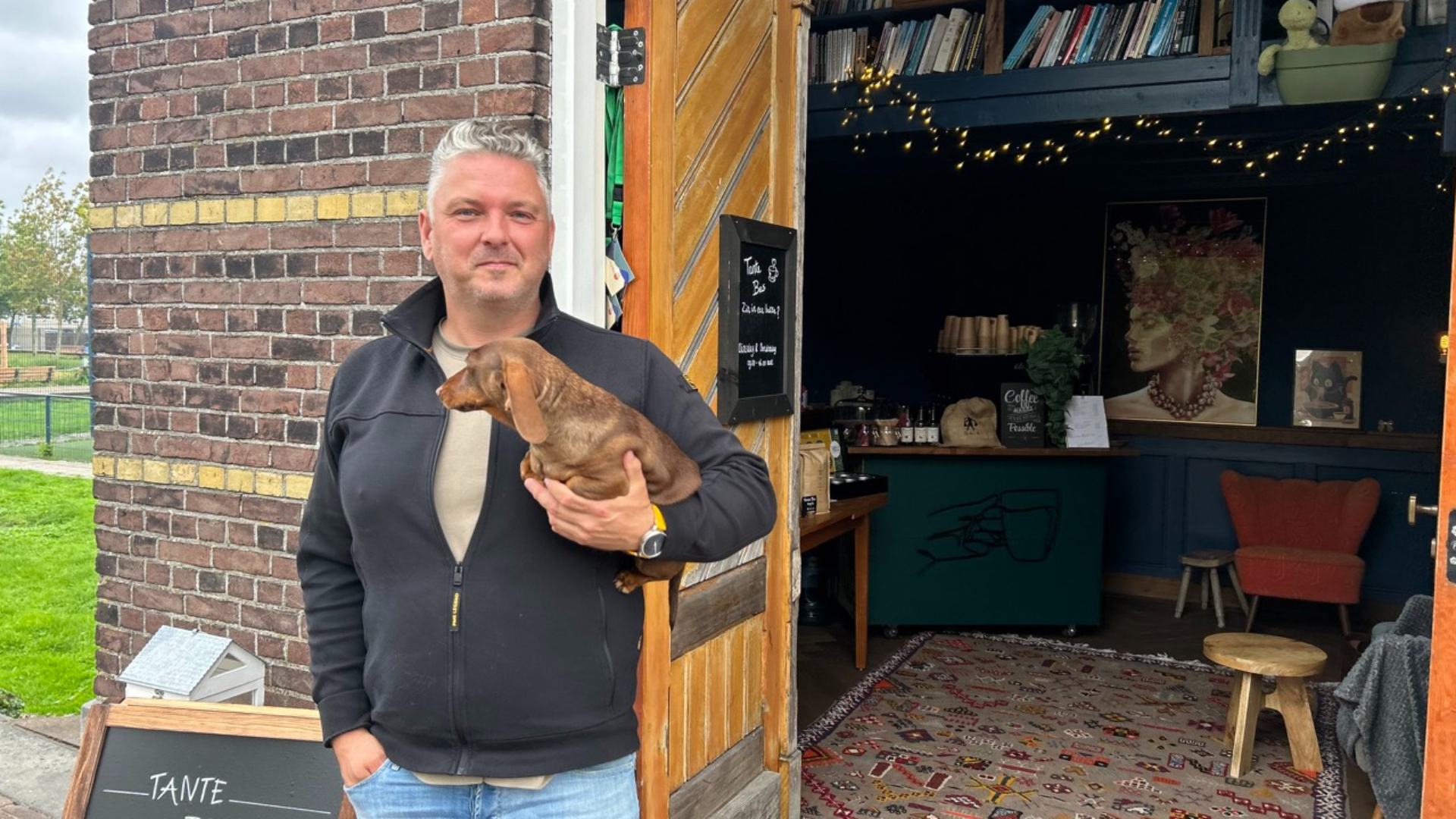 René met zijn bruine teckel, met op de achtergrond: de koffiebar en tientallen boeken