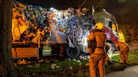 Vrachtwagen rijdt tegen boom; lading vuilnis ligt op de weg