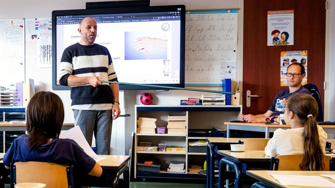 Een leraar legt aan basisschoolkinderen uit wat anderhalve meter is.