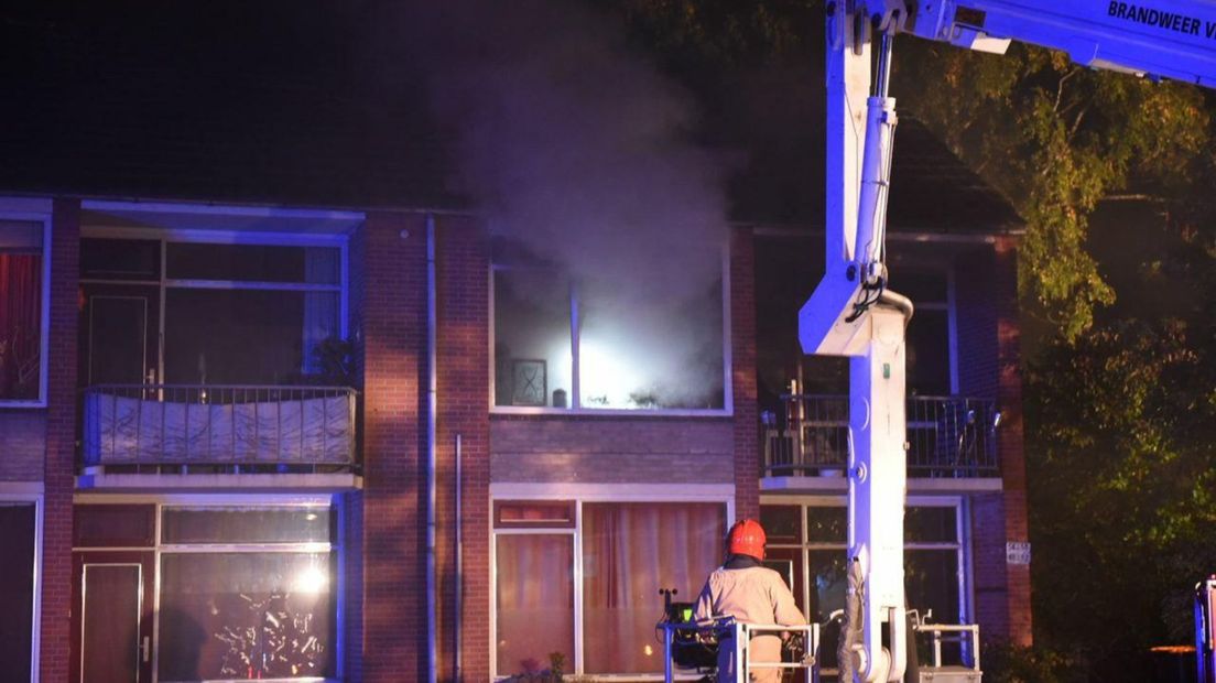 Een brandweerman laat zich met een hoogwerker richting het appartement takelen