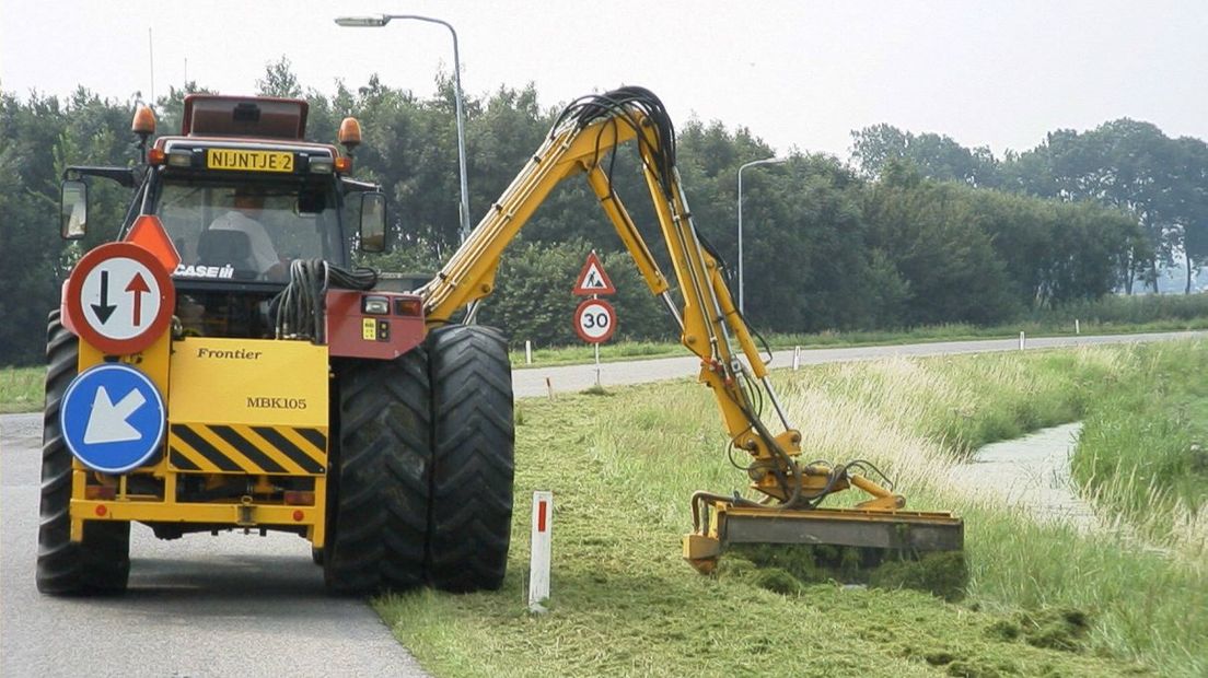 Een trekker maait de berm.