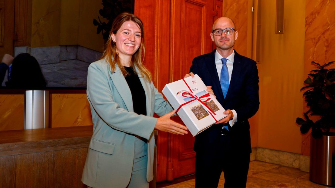 Wethouder Susanne Schilderman overhandigt de begroting aan raadslid Has Bakker (Beide D66)