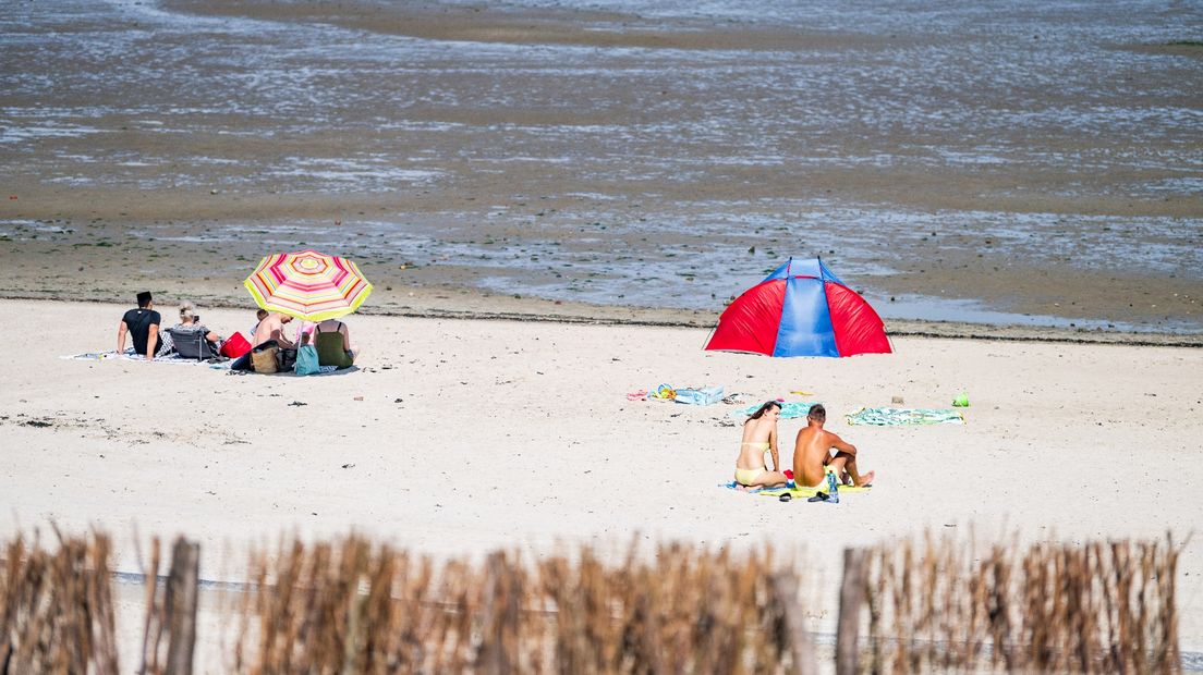 Mensen genieten van het zomerweer op het strand van Delfzijl.