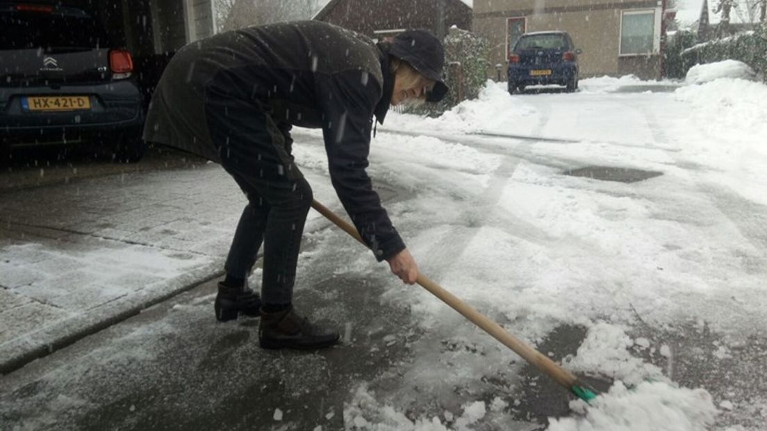 Een vrouw maakt de stoep sneeuwvrij.