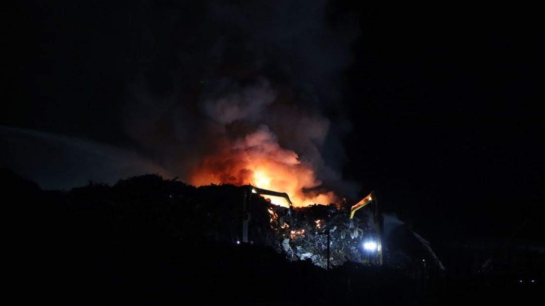 Kraan met grijper trekt brandende berg ijzer uit elkaar