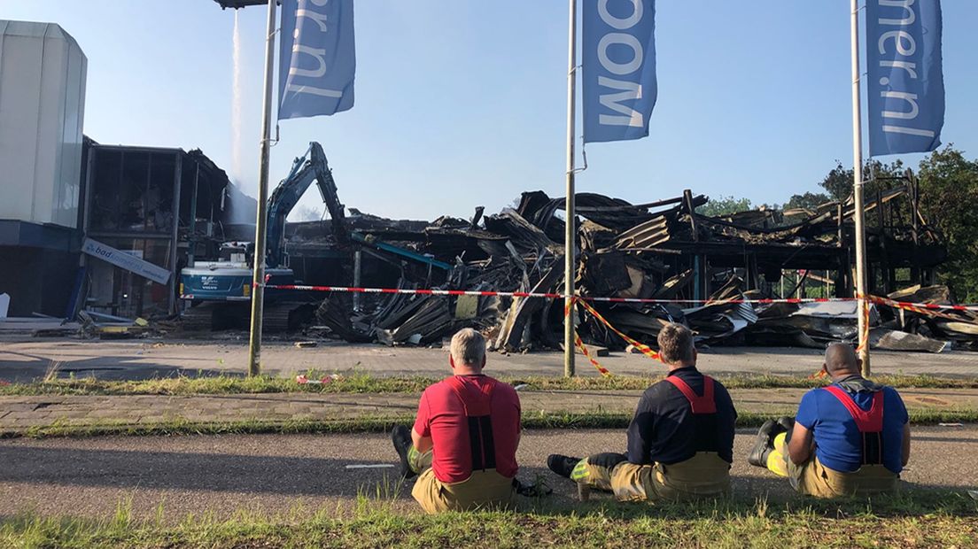 Brandweermedewerkers kijken de ochtend na de brand naar de puinhopen van de vuurzee.