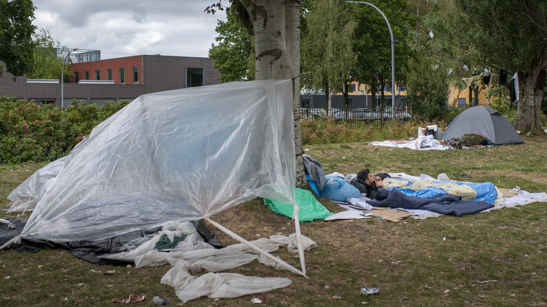 Asielzoekers houden zichzelf uit de wind met een geïmproviseerde tent bij Ter Apel zaterdag