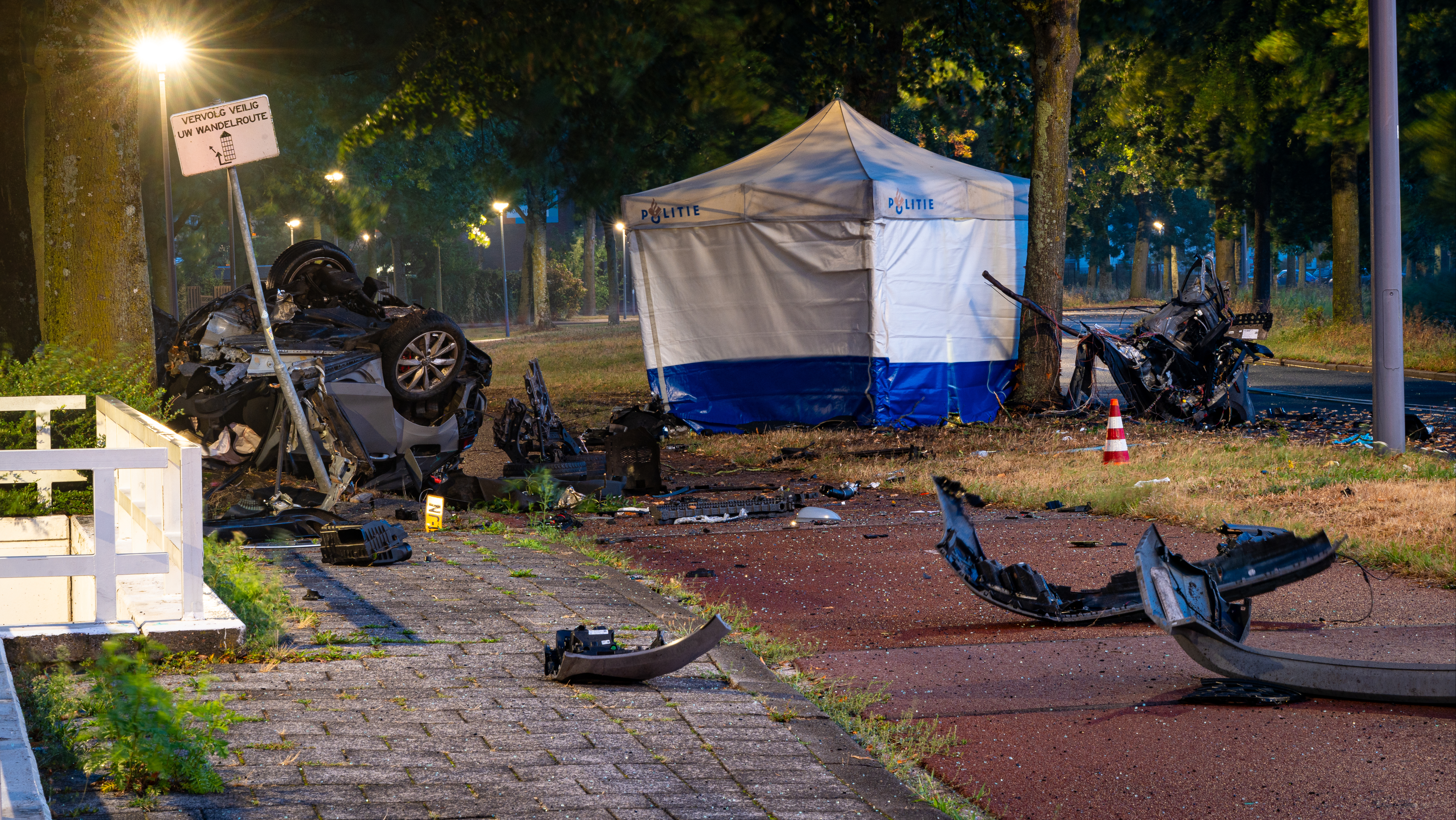 Wat er nog over is van de auto ligt verspreid over het gras en de weg.