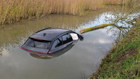 Auto rijdt boom uit de grond en komt in water terecht
