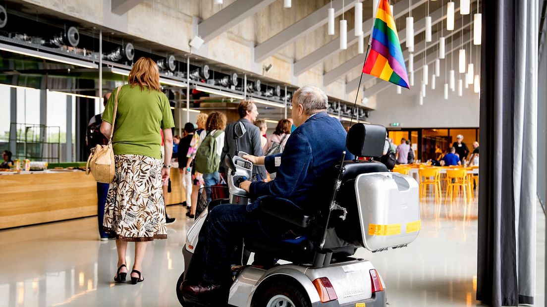 Een bejaarde man met een lhbti-vlaggetje op zijn scootmobiel
