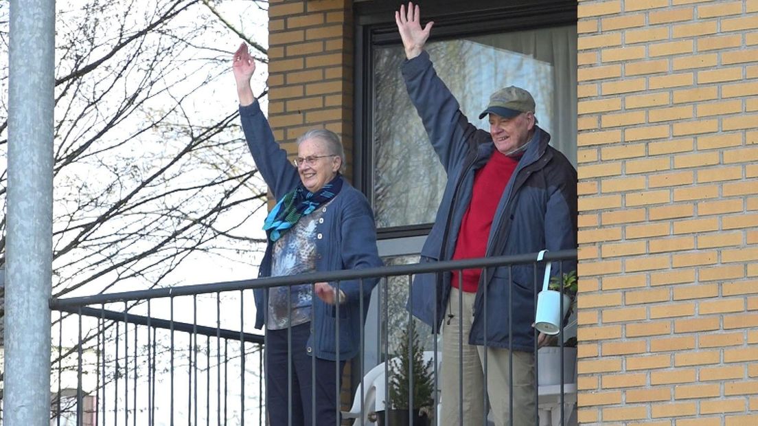 Twee bewoners van een zorgcentrum zwaaien op hun balkon.