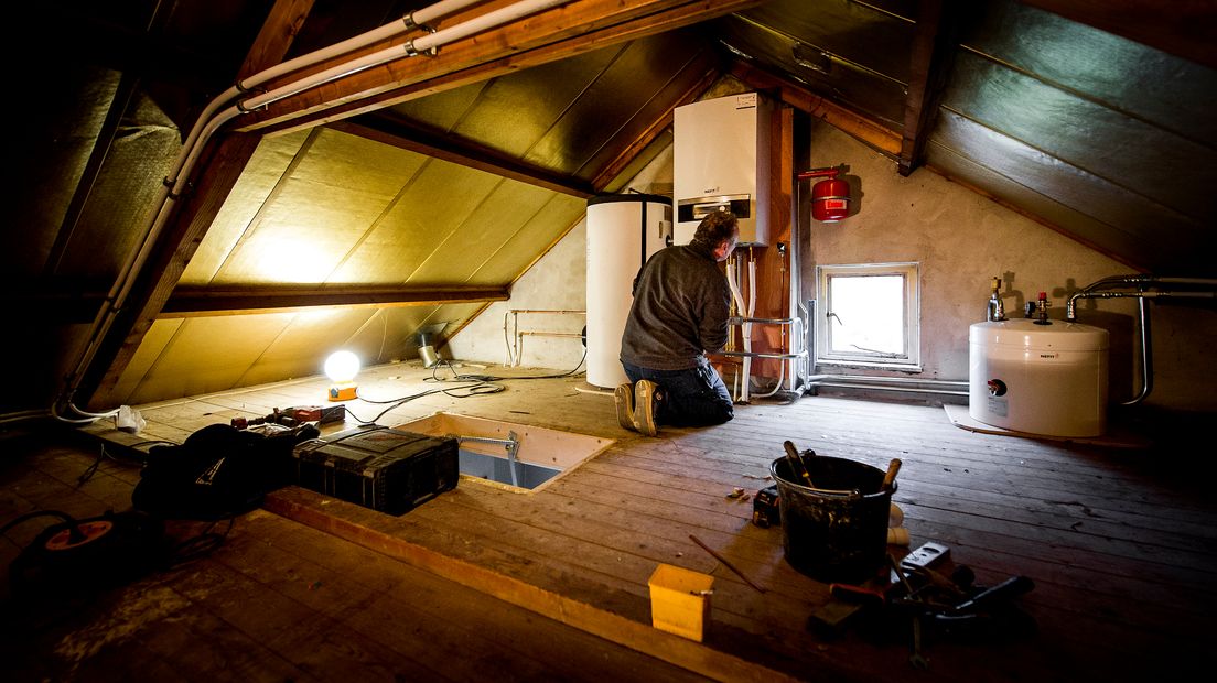 Een monteur is op een zolder bezig met de installatie van een warmtepomp