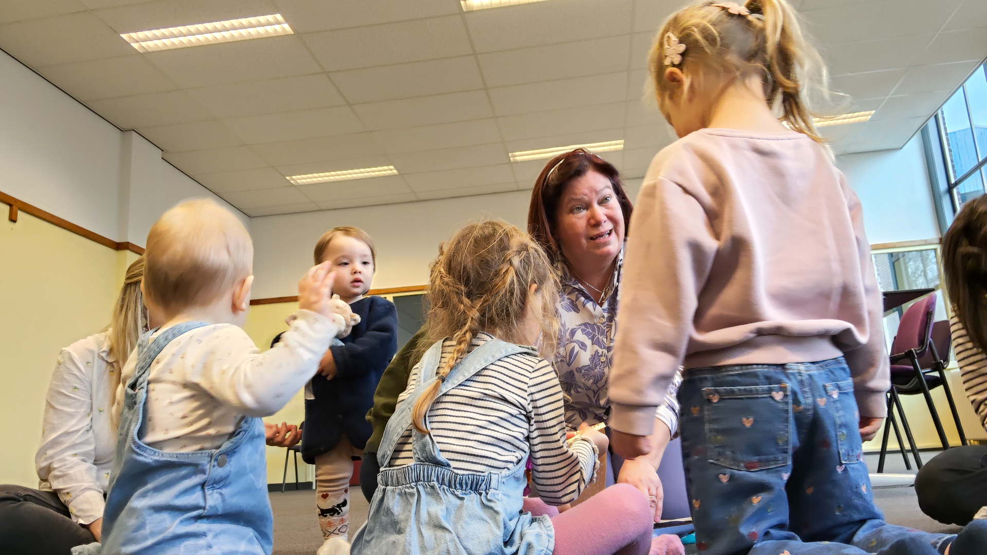 Enkele peuters zitten om juf Angelique heen tijdens een van de liedjes