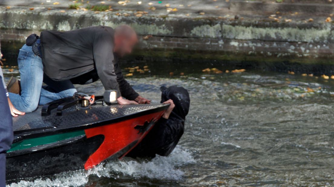 Een van de tegendemonstranten klampt zich vast aan de boot van De Ooievaart nadat hij te water is geraakt. 