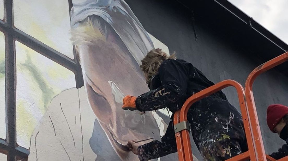 Een lid van De Strakke Hand werkt aan de muurschildering.