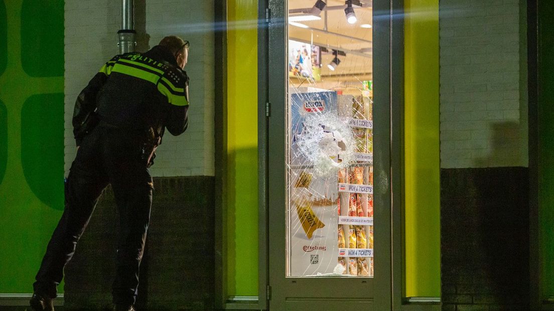 Een agent bekijkt de kapotte ruit van de Plus supermarkt